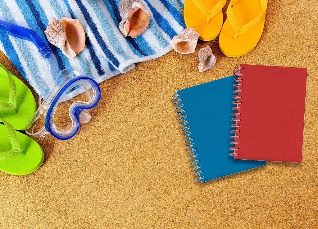 Cadernos, chinelos, conchas, e toalhas sobre a areia da praia