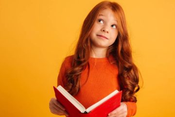 menina em pé segurando um livro com as duas mãos e pensando