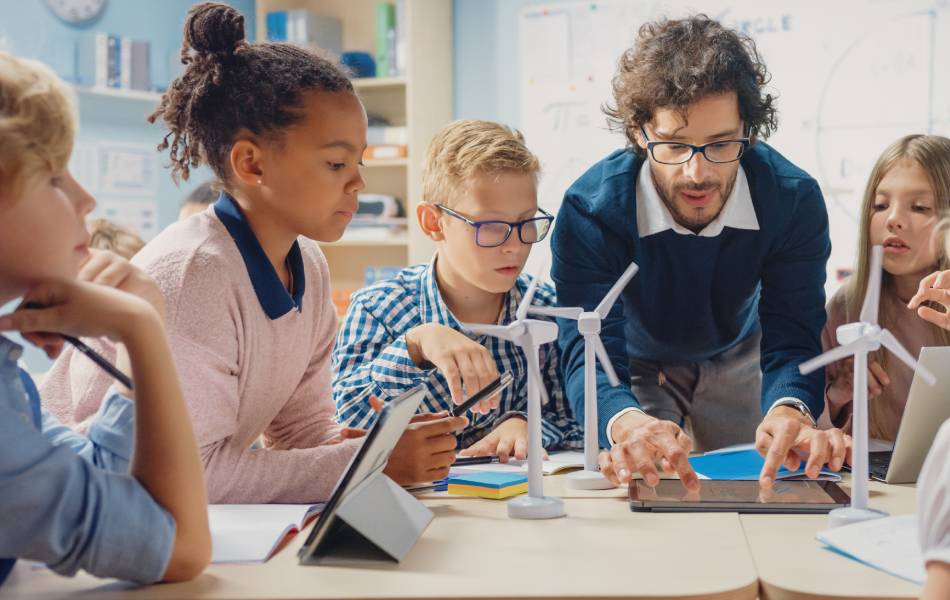 professor rodeado de alunos em uma mesa dando aula sobre tecnologia