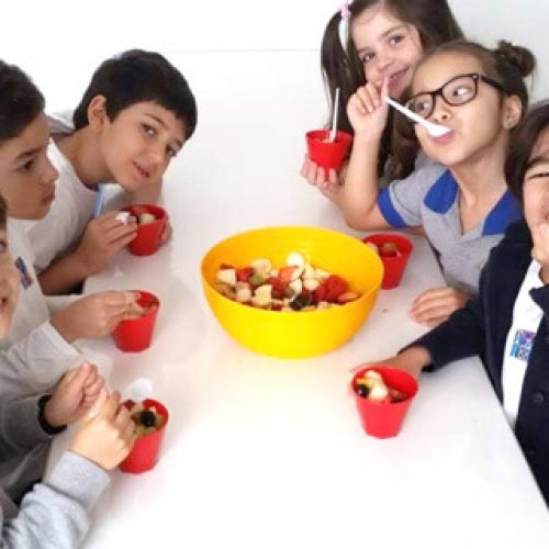 Grupo de criança em torno de uma mesa comendo frutas