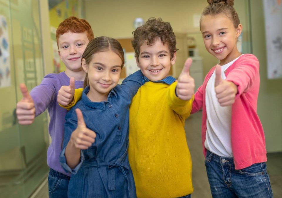 Crianças no corredor de uma escola bilingue fazendo sinal de "jóia", afirmando que está tudo bem!