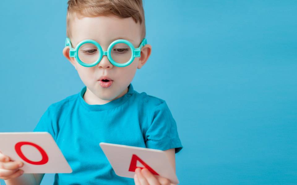 Menino olhando para letras de papel em suas mãos durante processo de alfabetização